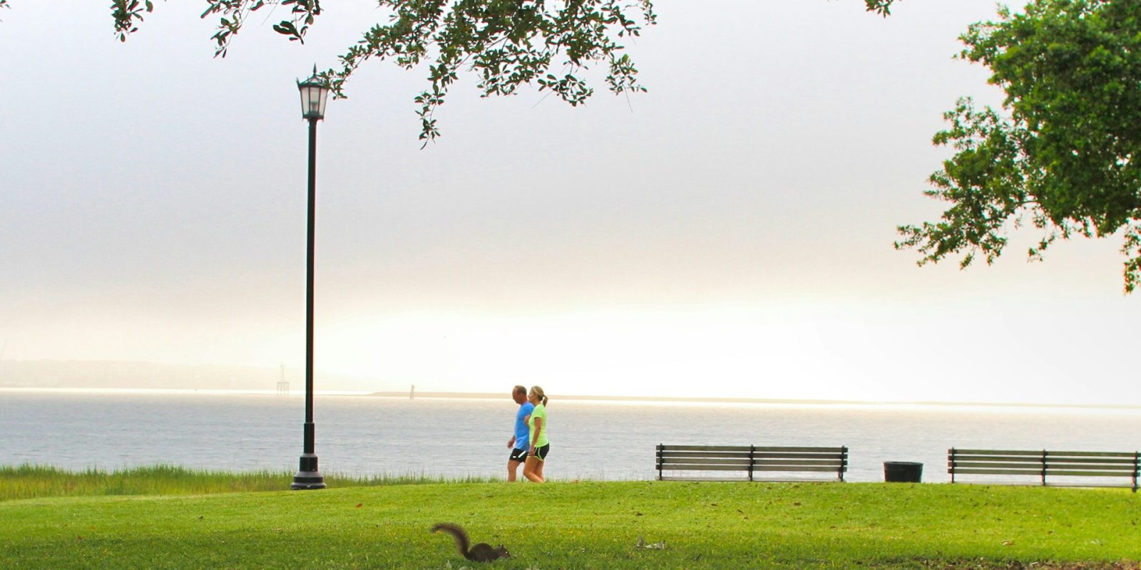 A couple of sports gear walk alongside a park against a sea views backdrop.