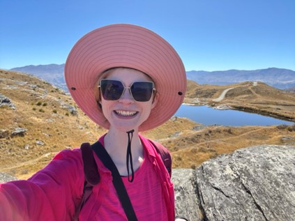Lady in pink straw hat and sunglasses against New Zealand's scenery.