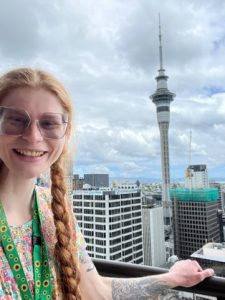 Young woman (Ailidh) smiling. In the background is the Sky Tower, Auckland.