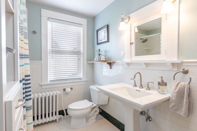 A light and airy bathroom with a sink in the foreground and a toilet next to it.