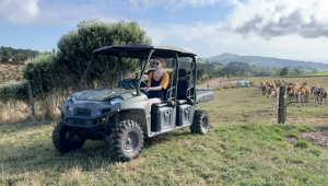 A young woman drives a Jeep across farmland with cattle in the background.