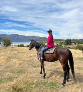 A woman on horseback riding through New Zealand's countryside.