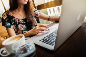 A young woman types on her laptop in a relaxed setting. Her face is not shown.