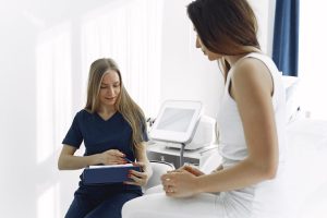A nurse talks to a patient. They are both seated and in a clinical setting.