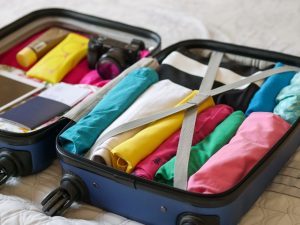 An open suitcase full of colourful clothes neatly packed in rolls.