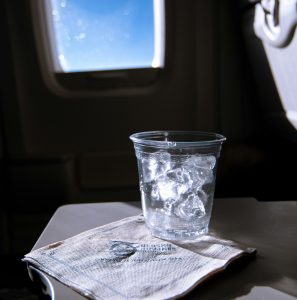 A plastic cup of ice cubes on a tray table, with a serviette underneath.