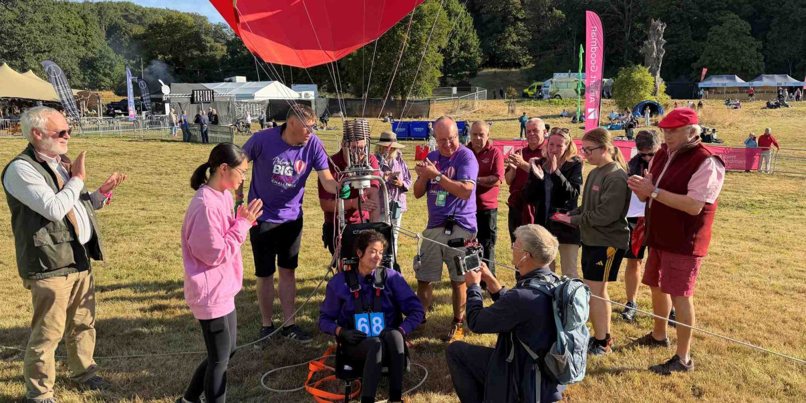 Hot air balloon pilot Jo Bailey seated beneath a balloon with a crowd of friends and family and a journalist before attempting a world record challenge in a field.