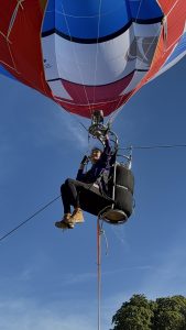 Jo Bailey ascends in her small 'hopper balloon' as part of a Guinness World Records challenge. Blue skies and a red and white air balloon.