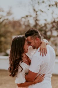 A smiling man and woman dressed in white embrace.