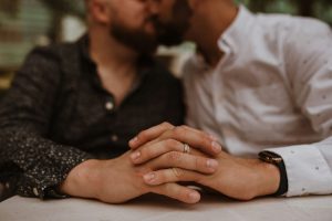 Two men kiss and hold hands. The focus is on their clasped hands.