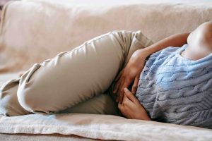 Woman lies on a sofa and holds her stomach, potentially in some pain.