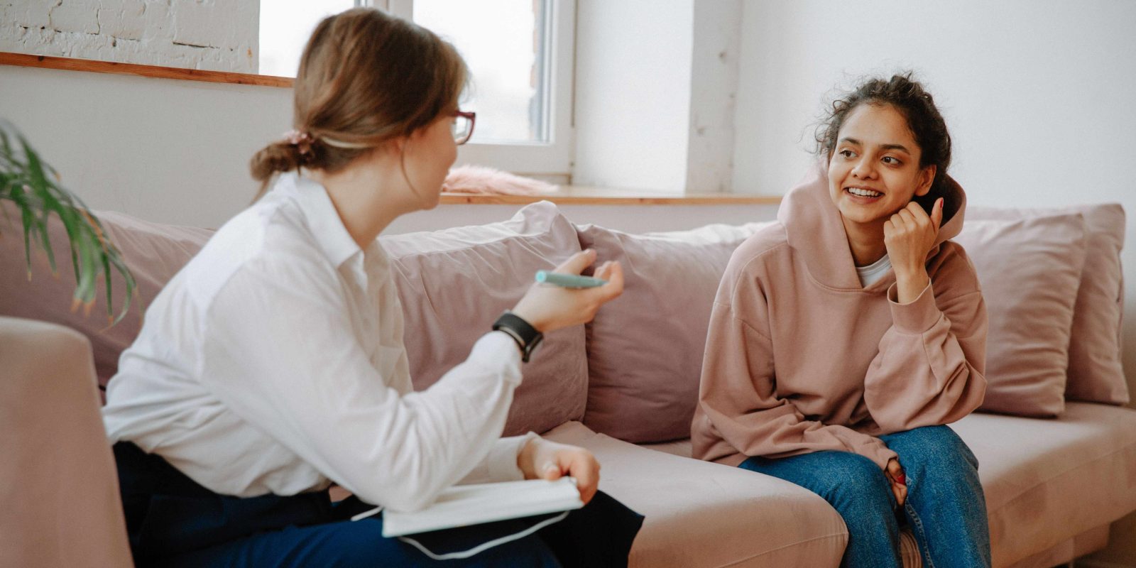 Two women sit on a sofa having a discussion, one is a therapist.