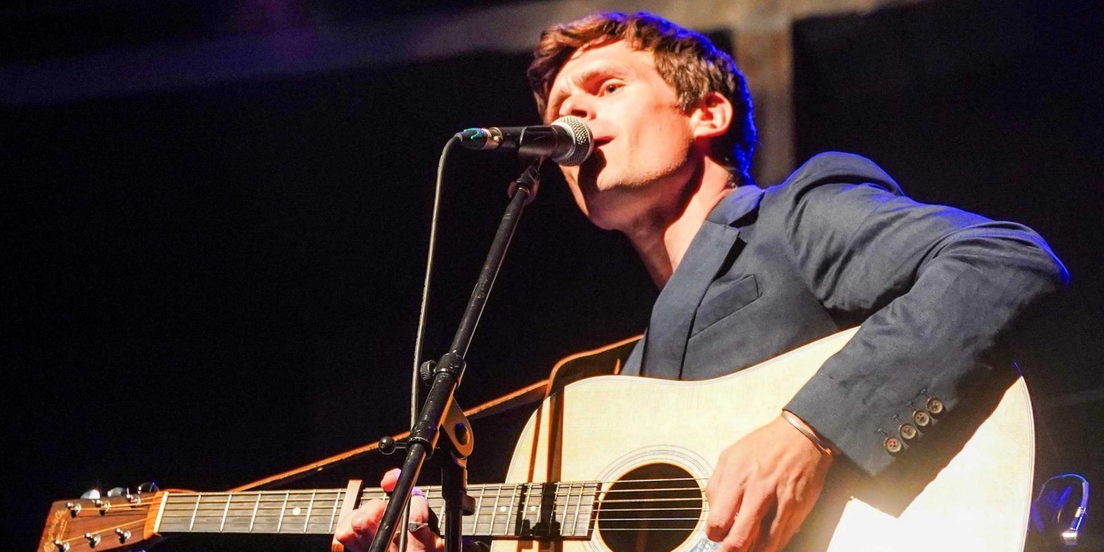 Tom Speight sings and plays guitar on stage.