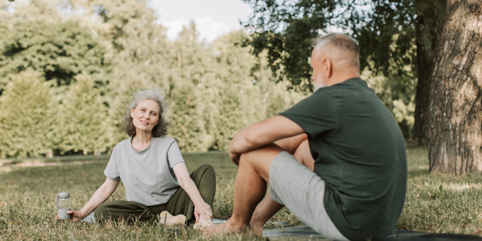 Senior couple practicing yoga and enjoying nature in a sunny park.